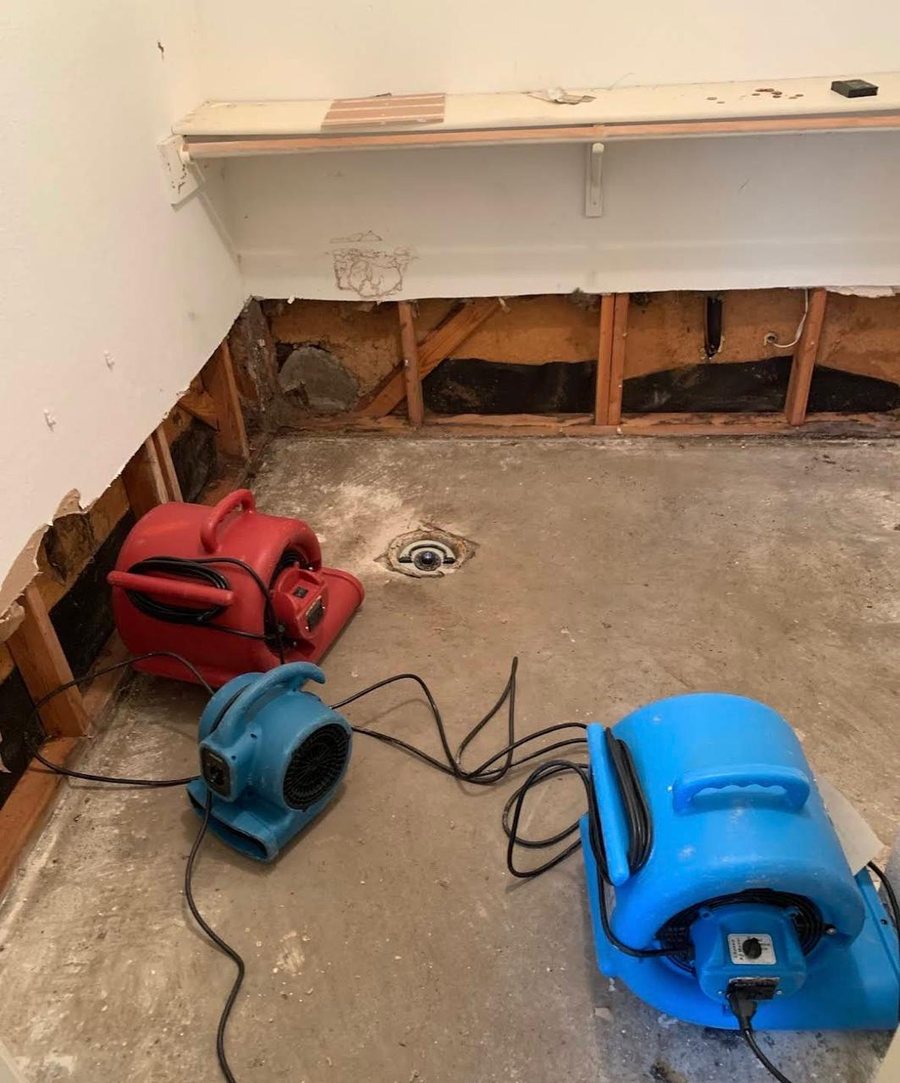Air movers and dehumidifiers running in flood-damaged Miami room with exposed walls
